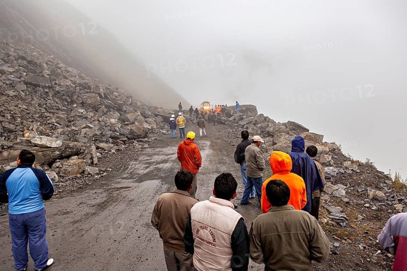 Several people watch a tractor in a foggy mountain landscape on a rocky road, rockslide on the pass road towards Rurrenabaque through the Andes on the Road of Death in Bolivia