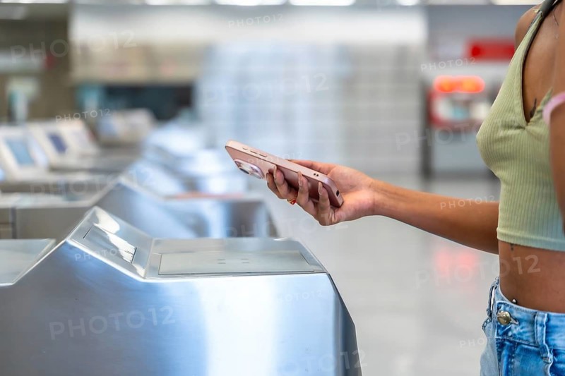 Woman using contactless mobile payment at a subway turnstile, entering the station during her daily commute, representing modern urban travel technology and convenience
