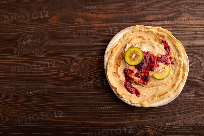 Stack of Plain Fried pancakes with jam and kiwi on brown wooden. top view, flat lay, copy space