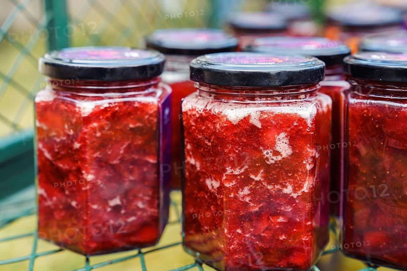 Fresh strawberry jam, rolled up in jars, stands in a mesh metal box. Farm natural products. Conservation and preparations
