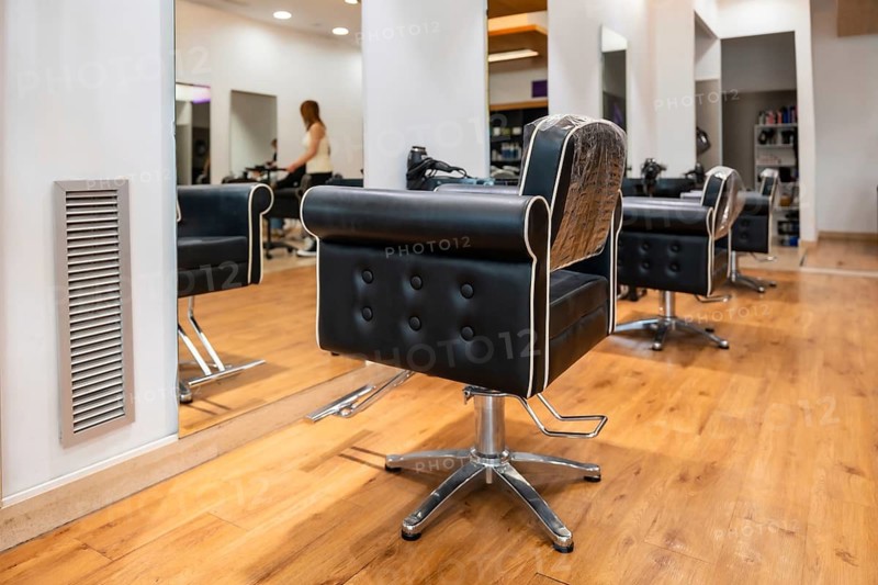 Hair salon interior featuring empty black leather styling chairs with white piping, reflective wall mirrors, and a warm wooden floor, symbolizing professional beauty and grooming services