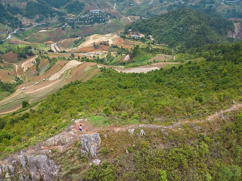 Aerial view of a woman with a pink rucksack walking along The Dinosaur Backbone (S?ng Lung Kh?ng Long), De Xu Phinh Commune, across rice terraces whilst the new, fresh green rice is being planted, the new, fresh green rice seedlings at Mù Cang Ch?i, Mu Cang Chai District, Lào Cai Province, Northern Vietnam, Vietnam
