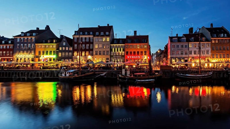 Bunte, beleuchtete Fassaden spiegeln sich nachts im Wasser eines belebten Kanals, Kopenhagen, Dänemark, Nyhavn