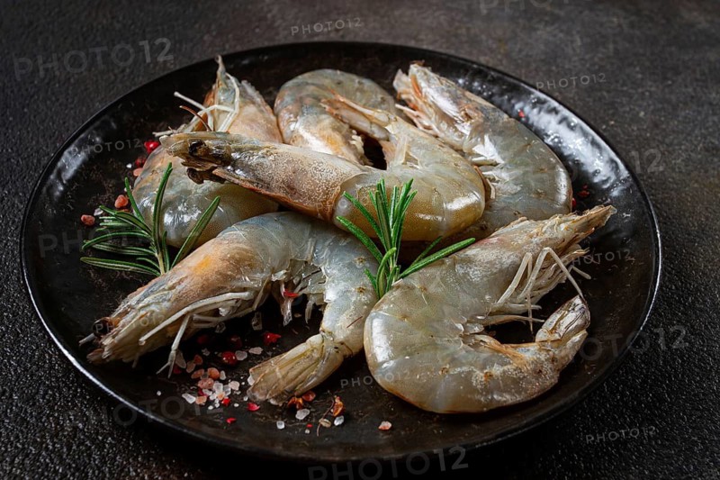 Fresh raw white-footed shrimp, tiger prawns vannamei, on a black plate, with spices and herbs