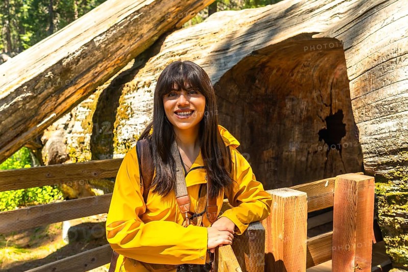 Young woman smiling while visiting the massive fallen giant sequoia tree, fallen monarch, in sequoia national park, enjoying her nature travel experience