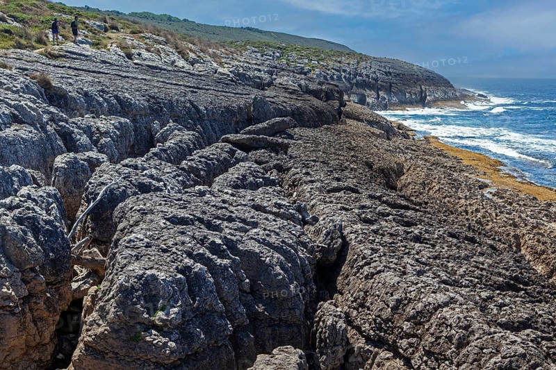 A couple of hikers walk by San Vicente cliffs along the coast trail near San Vicente de la Barquera, Santander, Cantabria, Spain
