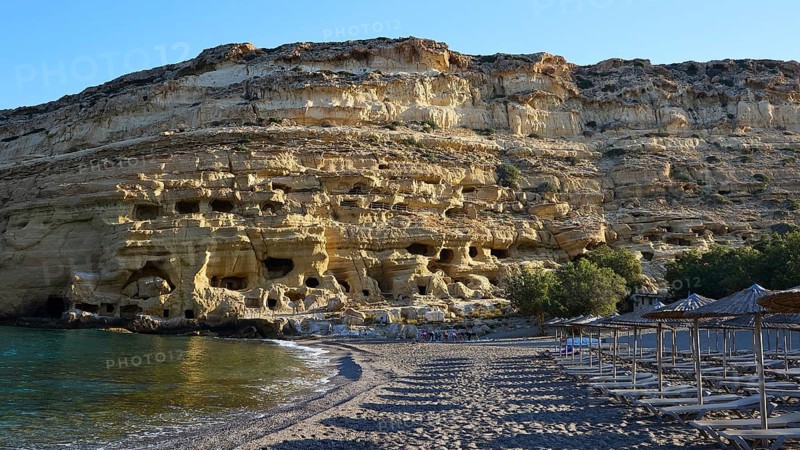 Neolithic caves, former hippie paradise, sandy beach with impressive rocks and empty umbrellas against a clear blue sea, Matala, south coast, Crete, Greek islands, Greece