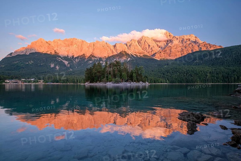 Beautiful sunset glow over the Maximiliansinsel island at Eibsee lake with Zugspitze mountain peaks and rocky foreground in Bavaria, Germany