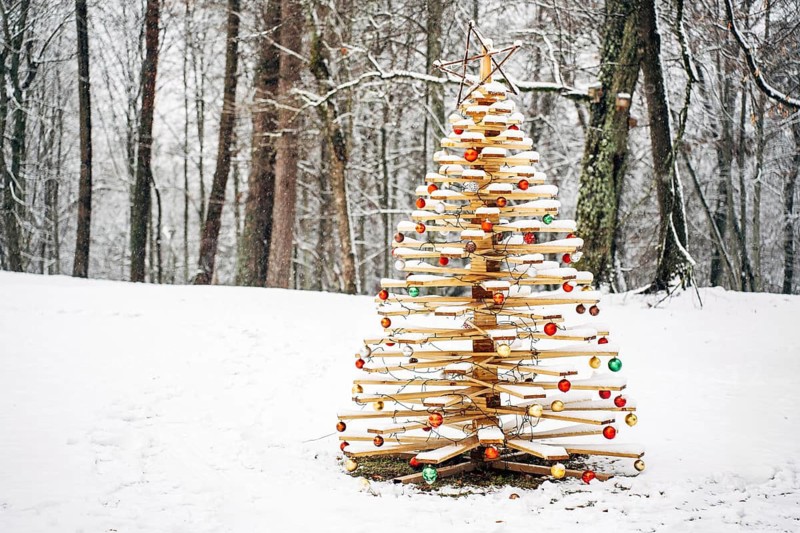 Beautiful handmade wooden Christmas tree decorated with festive balls in a snowy forest in winter