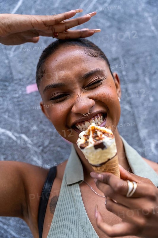 Happy young woman eating an ice cream cone with great delight, expressing pure joy and refreshment during a warm summer day against a textured urban background