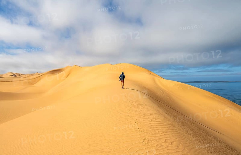 Lonely person, man with camera running on a dune, sand dunes and sea, Atlantic coast and sandy desert with sea of dunes, Sandwich Harbour, Namib Naukluft Park, Namib Desert, Namibia