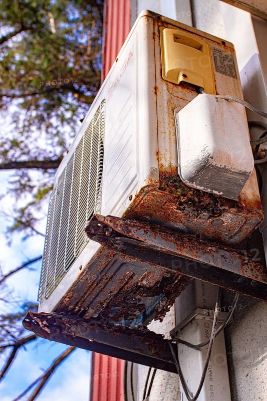 An old and rusty air conditioner hanging on the hotel building, in the sunny outdoor, seaside resort