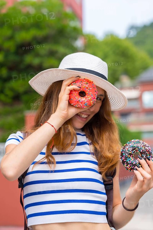 Young woman in a straw hat and striped shirt holding two colorful donuts