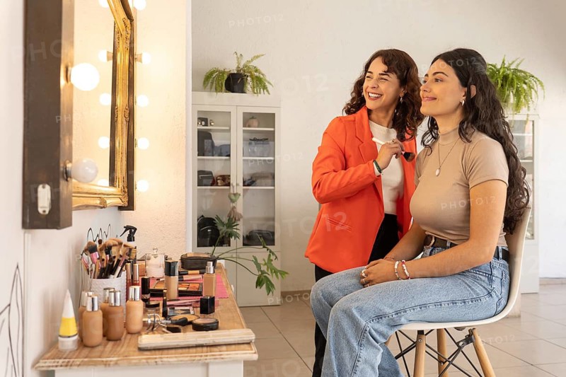 Makeup artist and client share a joyful moment and laugh together after a completed makeup session in a bright beauty salon