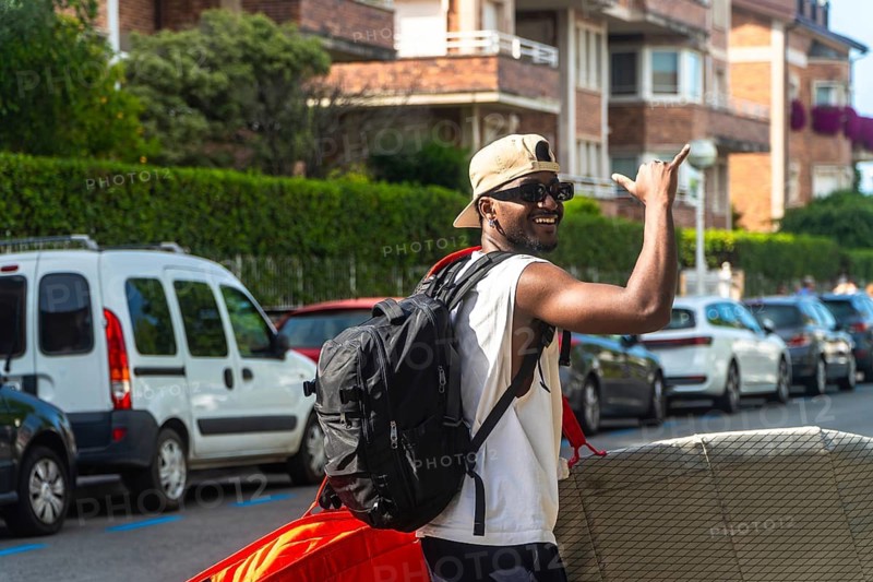 Young black man smiling and signaling shaka with beach equipment, enjoying summer lifestyle and vacation travel in a urban environment