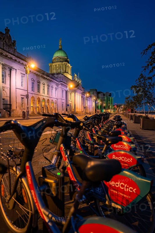 Row of rented bikes in front of illuminated historic and modern buildings, Dublin, Ireland