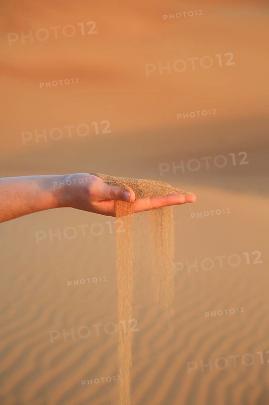 Sand flows gently from an outstretched hand in a quiet dune desert, a woman's hand lets red desert sand fall through her fingers and shows the connection with nature in the landscape, desert, sunrise, Dubai, United Arab Emirates