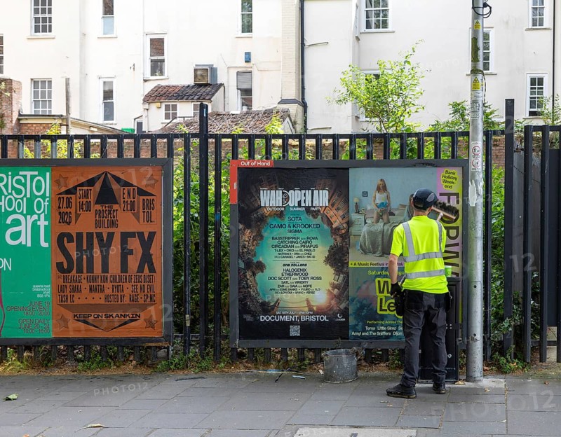 Man brushing vent poster onto advertising board space in city centre of Bristol, England, UK