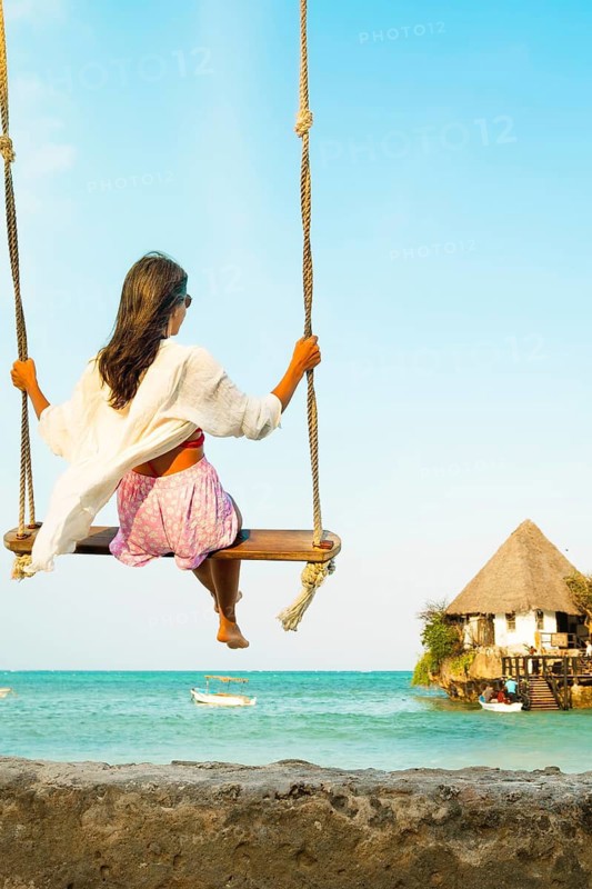 Traveler woman relaxing on swing above south beach in Zanzibar. Leisure tourist travel summer holiday vacation trip. Beautiful destinations place Africa. Happy dream concept