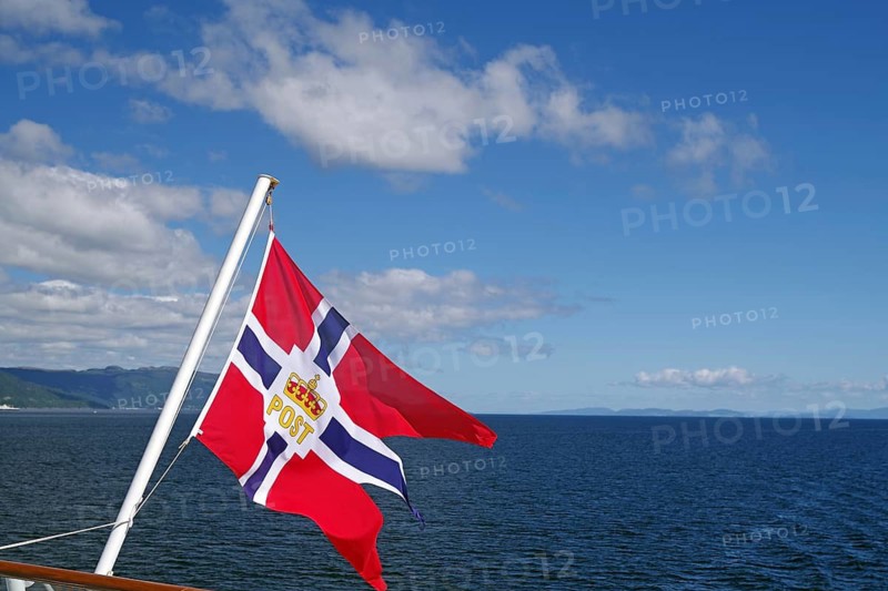 A Norwegian flag blowing in the wind over a clear blue sea and sky, mail ships, Havilla, Trondheim, Norway