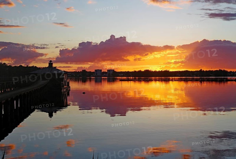 The sky glows orange and purple at sunset with clouds and reflections on the still water surface, Göta Canal, Karlsborg, Västra Götalands län, Sweden
