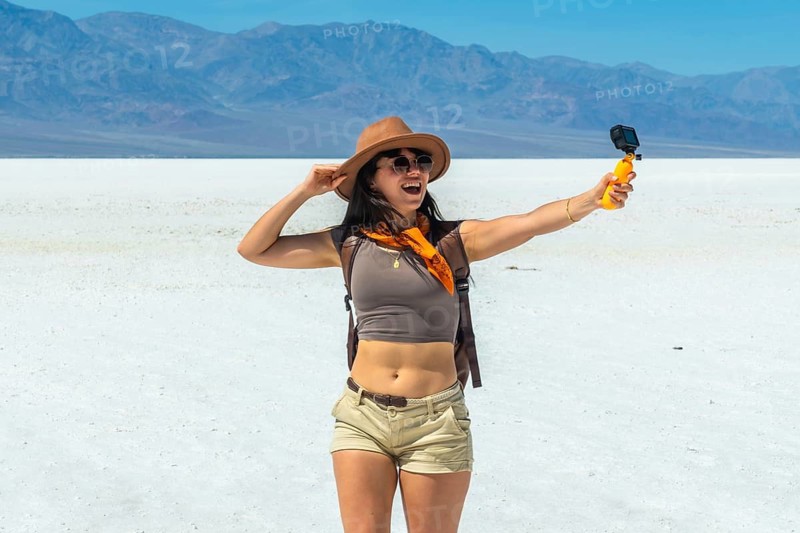 Young woman traveler smiling, recording herself with an action camera on a selfie stick across the vast salt flats of badwater basin, death valley national park