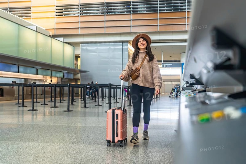 Woman smiling, walking confidently through a modern airport terminal pulling her suitcase, representing themes of travel, vacation, departure, and the beginning of a journey