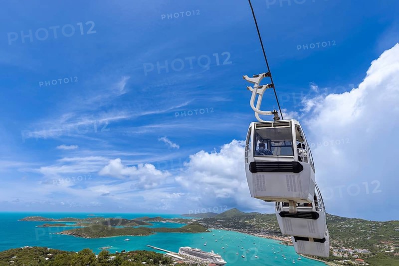 A cable car gondola rides above Charlotte Amalie harbor in St Thomas, US Virgin Islands, offering a panoramic view of turquoise water, green islands and a cruise ship below