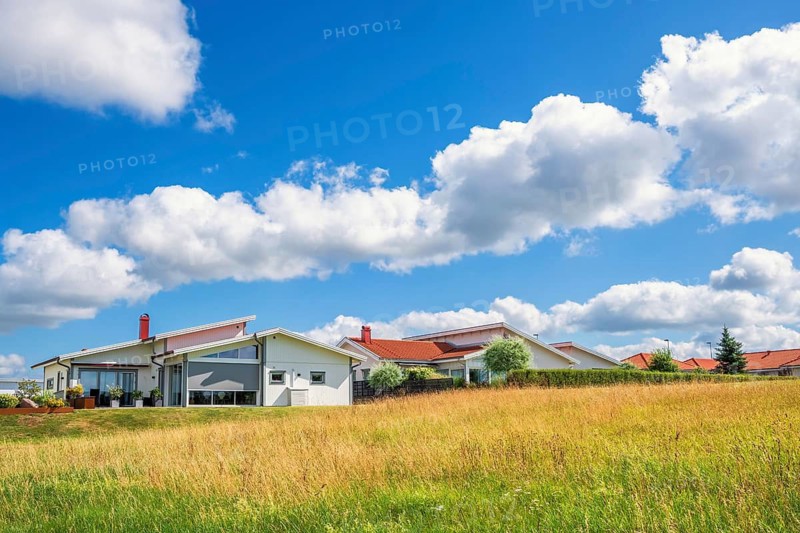 Modern residential house with large windows situated in an open grassy field under a bright blue sky with scattered clouds a sunny summer day, Falköping, Sweden