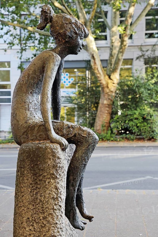 Girl sculpture on the wall by Clemens Pasch 1979 Modern art, bronze sculpture, life-size, child sitting on stone, Theaterstraße, Altstadt, Aachen, Eifel, North Rhine-Westphalia, Germany