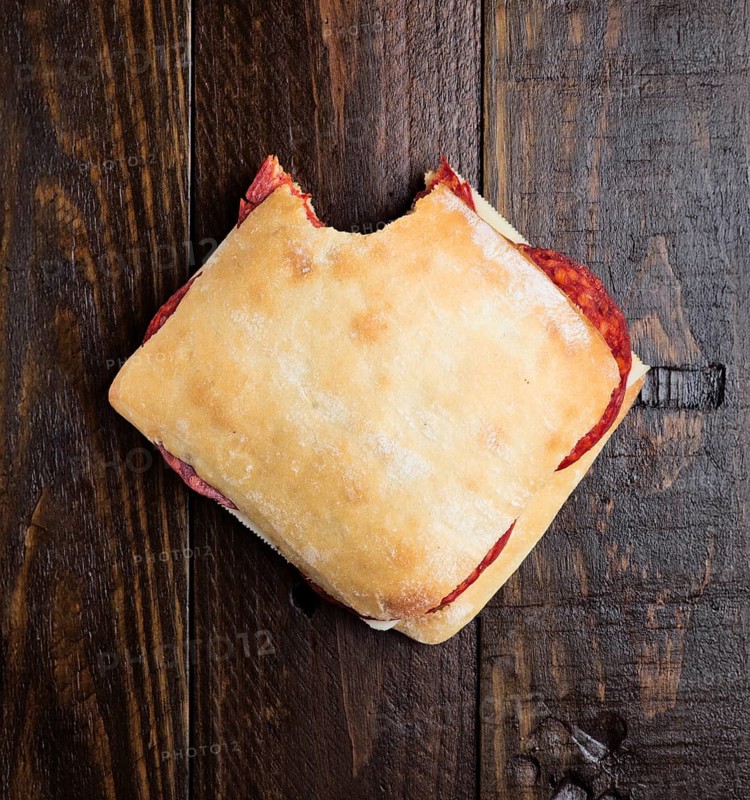 Top view of a homemade chorizo sandwich with a bite taken out, placed on a rustic wooden surface