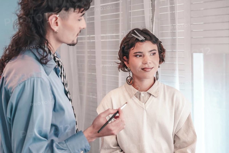 Professional makeup artist holding a brush and applying makeup on a model in a bright studio environment, showcasing diversity and inclusion