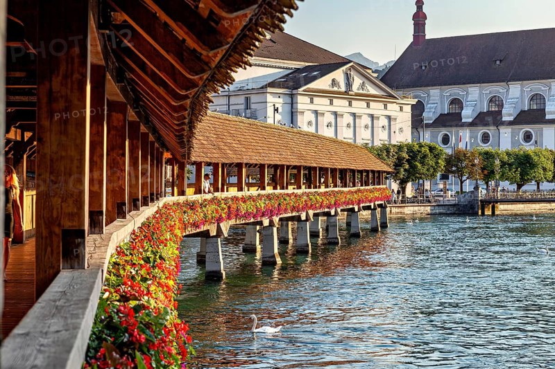 Historic wooden bridge decorated with flowers stretching across a river with old buildings in the background, The Chapel Bridge in Lucerne in Switzerland
