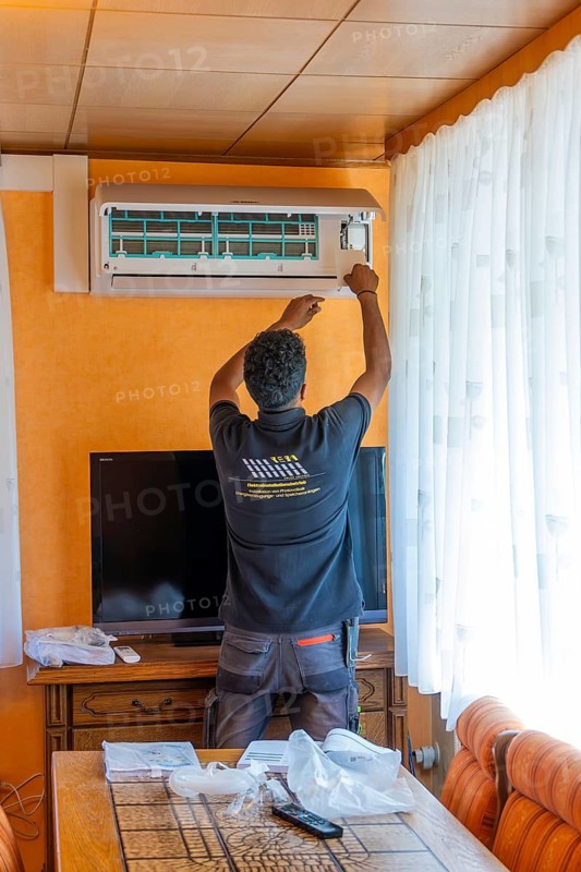 A man mounts an air conditioner over a television in the living room, air conditioning and refrigeration technology, private house, Wurmberg, Germany