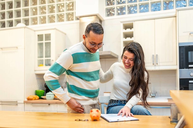 Young couple joyfully calculating savings, reviewing documents for financial planning and investment, and managing their household budget in a home kitchen