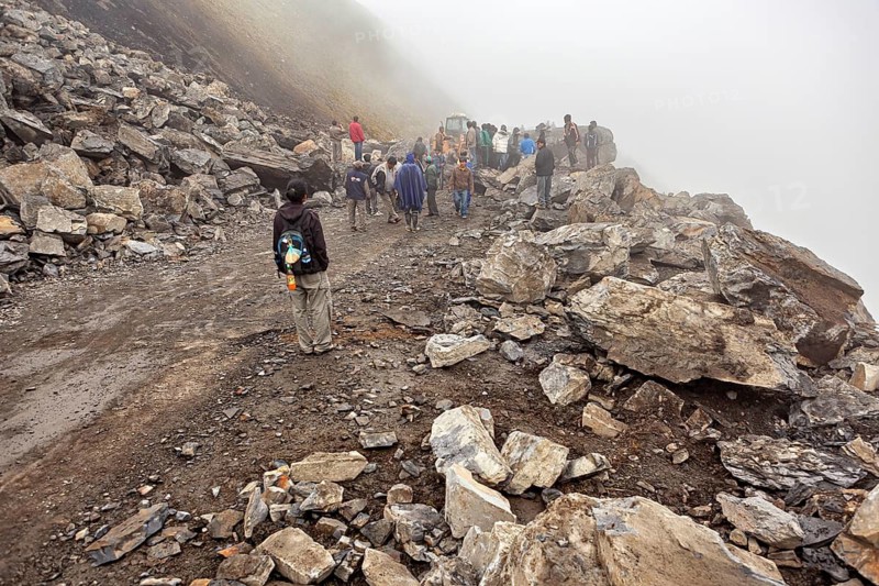 People on foggy road with rocks, some wearing protective clothing, unclear path, rockslide on the pass road towards Rurrenabaque through the Andes on the Road of Death in Bolivia