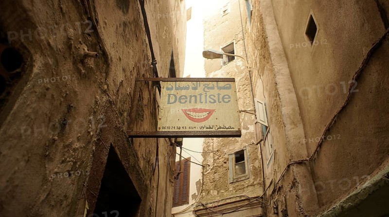A narrow alley with a sign from a dentist between old, mysterious buildings in the old town, Medina of Marrakech, Morocco