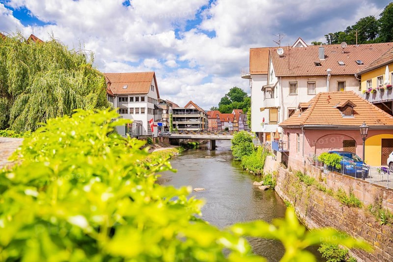 Summer day on a river with buildings and a bridge surrounded by green vegetation, Calw, Black Forest, Germany