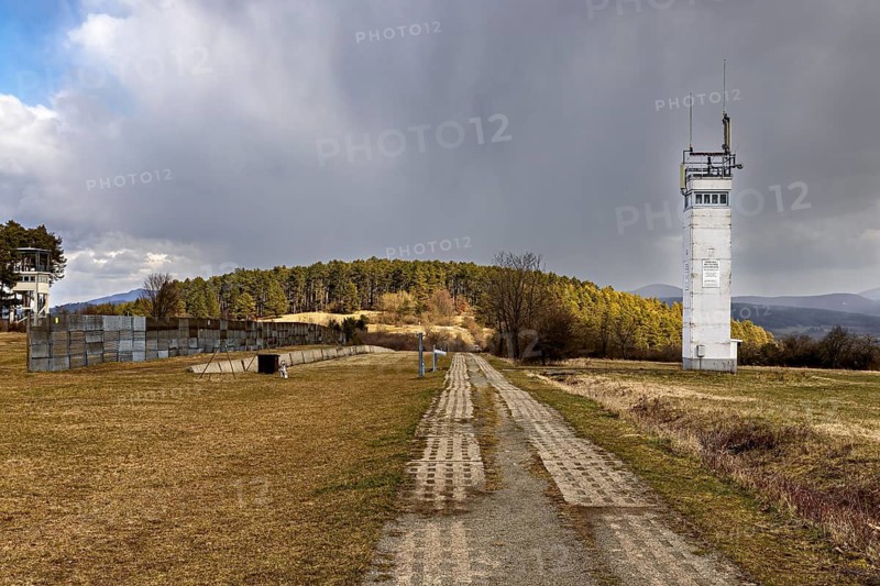 A white watchtower stands next to a long path in a meadow with a cloudy sky, the Point Alpha memorial between Rasdorf and Geisa in the Rhön