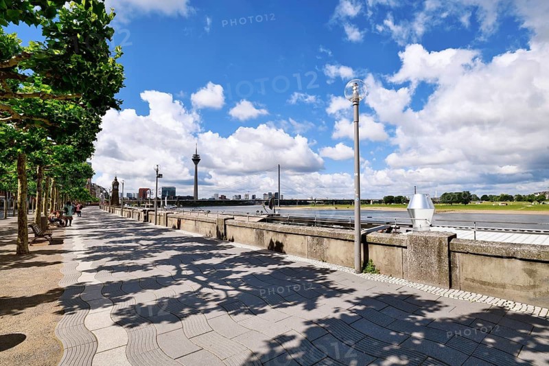 Düsseldorf, Germany - June 9th 2026: Riverside promenade 'Rheinuferpromenade' with Rhine River, opposite riverbank and Rheinknie Bridge on a sunny day