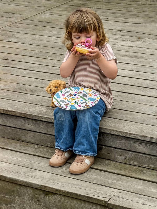 Little Caucasian girl, 3 years old, sitting on a wooden deck and eating a cake in Ystad, Skåne County, Sweden, Scandinavia