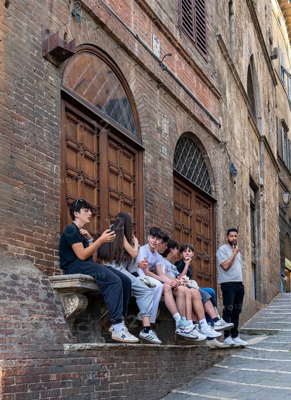 Group of teenagers sitting on a stone bench in Piazza del Campo, Siena, Tuscany, Italy