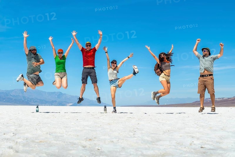 Group of friends jumping in the air with arms raised, celebrating adventure on the vast white salt flats under a clear blue sky, experiencing joy and freedom during desert travel