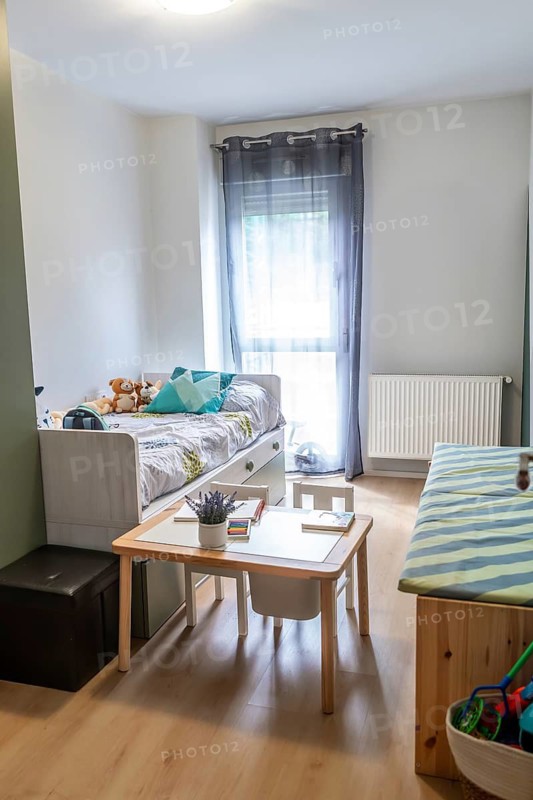Bright kids' bedroom showcasing a comfortable bed with storage drawers, a small wooden activity table with chairs, and various toys, creating a functional and cozy learning space for children