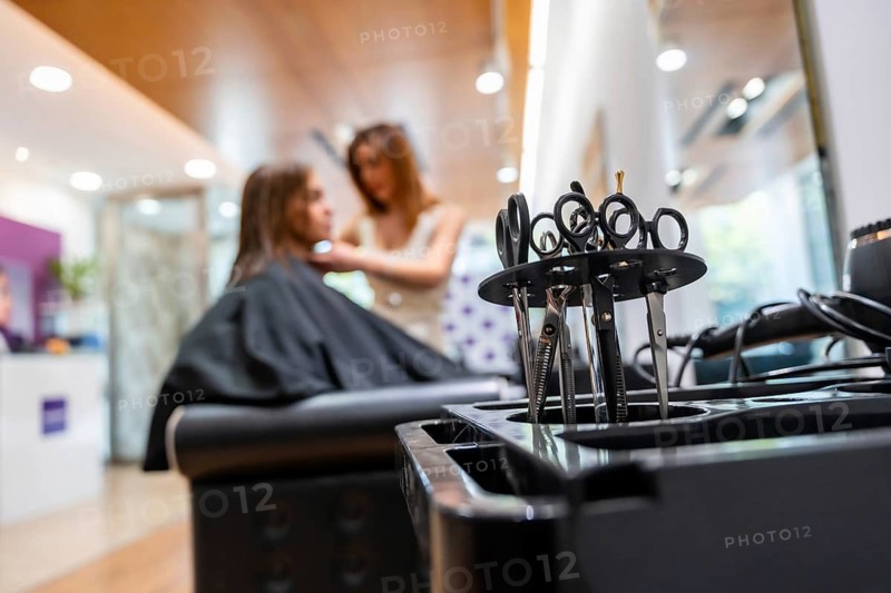 Hairdressing scissors and tools on a salon trolley in sharp focus while a female stylist attends a client in the blurred modern salon background, professional grooming scene