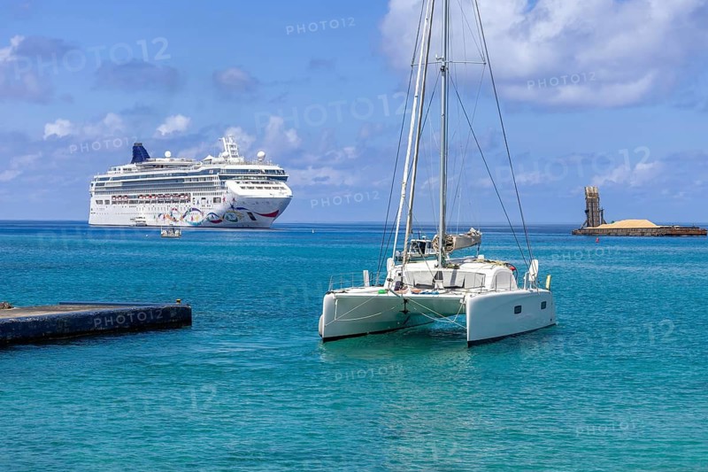 A catamaran sailboat moored in the clear turquoise Caribbean Sea along the rocky tropical waterfront of George Town in the Cayman Islands vacation destination