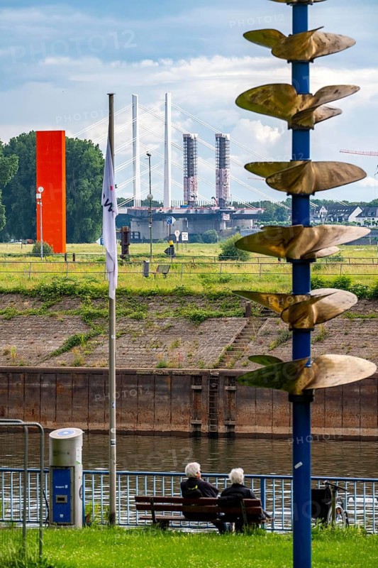 Promenade at the port of Duisburg-Ruhrort, Vincke Canal, Inland-Hafen-Tor sculpture by Günter Schirmer, view over the bank of the right bank of the Rhine near Duisburg-Kasslerfeld and Ruhrort, Rhine orange sculpture at the mouth of the Rhine, in the background the Neuenkamp motorway bridge, A40, construction site of the 2nd construction phase, North Rhine-Westphalia, Duisburg