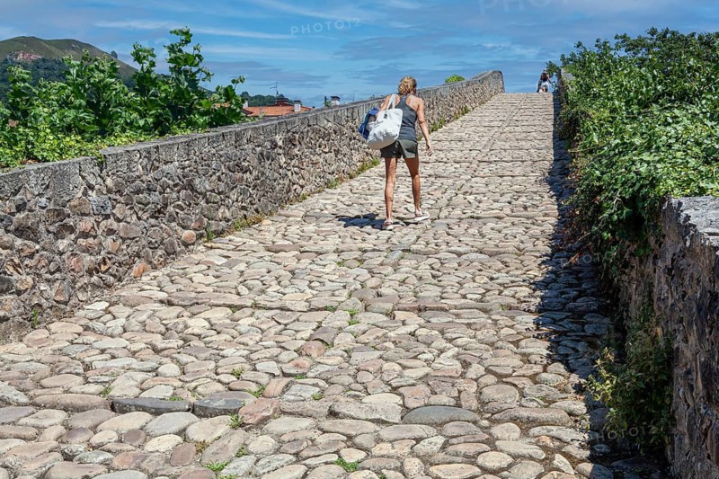 Middle aged woman walks up the roman bridge in Cangas de Onis village, principality of Asturias, Spain