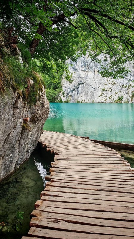 A wooden walkway winds along a turquoise lake, framed by rocks and trees, Plitvice Lakes National Park, Croatia