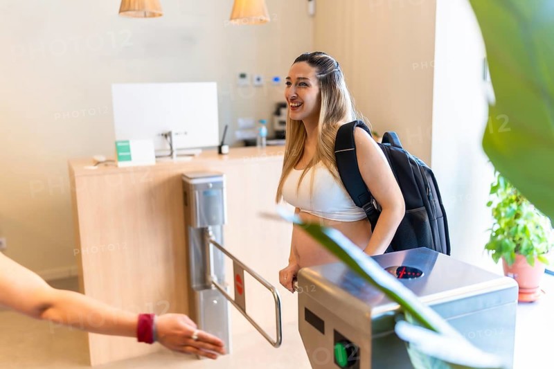 Pregnant woman smiling while passing through a turnstile at the gym entrance, getting ready for prenatal fitness and maintaining an active, healthy lifestyle during pregnancy